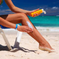 Woman Putting on Sun Screen on her legs at the beach