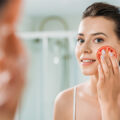 Young woman rubbing tomato onto her face
