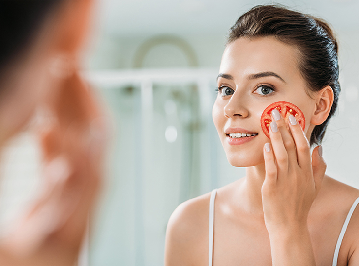 Young woman rubbing tomato onto her face